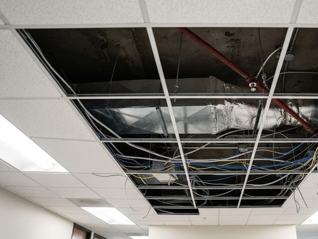 Open ceiling grid showing ductwork, conduit and data cable above